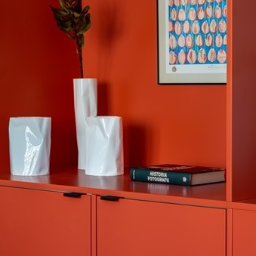 Fresh Home - Czerwona szafka z trzema białymi wazonami o nieregularnych kształtach, książką 'Historia Fotografii' i abstrakcyjnym obrazkiem na ścianie w dopasowanym kolorze.