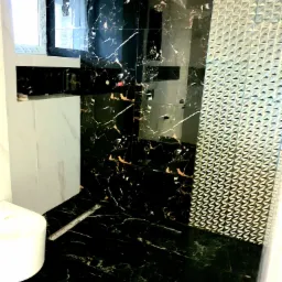 Wykończona łazienka z czarnymi płytkami imitującymi marmur z białymi żyłami, srebrną mozaiką 3D i białą armaturą, widoczny odpływ liniowy i okno.