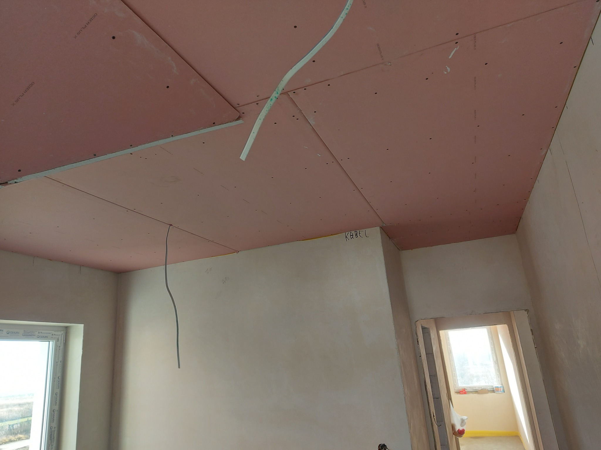 Montaż płyt kartonowo-gipsowych na suficie, widoczne kable elektryczne i fragment ściany z napisem 'KABEL'.