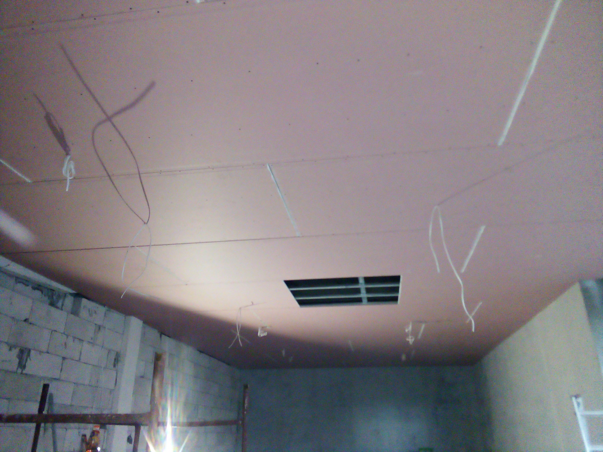 Sufit z płyt kartonowo-gipsowych w trakcie montażu, widoczne przewody i otwór wentylacyjny, ściany z pustaków.