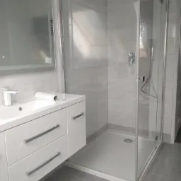 Nowoczesna łazienka z kabiną prysznicową typu walk-in, białą szafką z umywalką i lustrem z podświetleniem LED, wykończona szarymi płytkami.