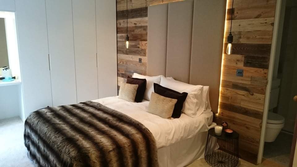 Sypialnia z łóżkiem, drewnianą ścianą z podświetleniem LED, wiszącymi lampami żarowymi i szafą w zabudowie.