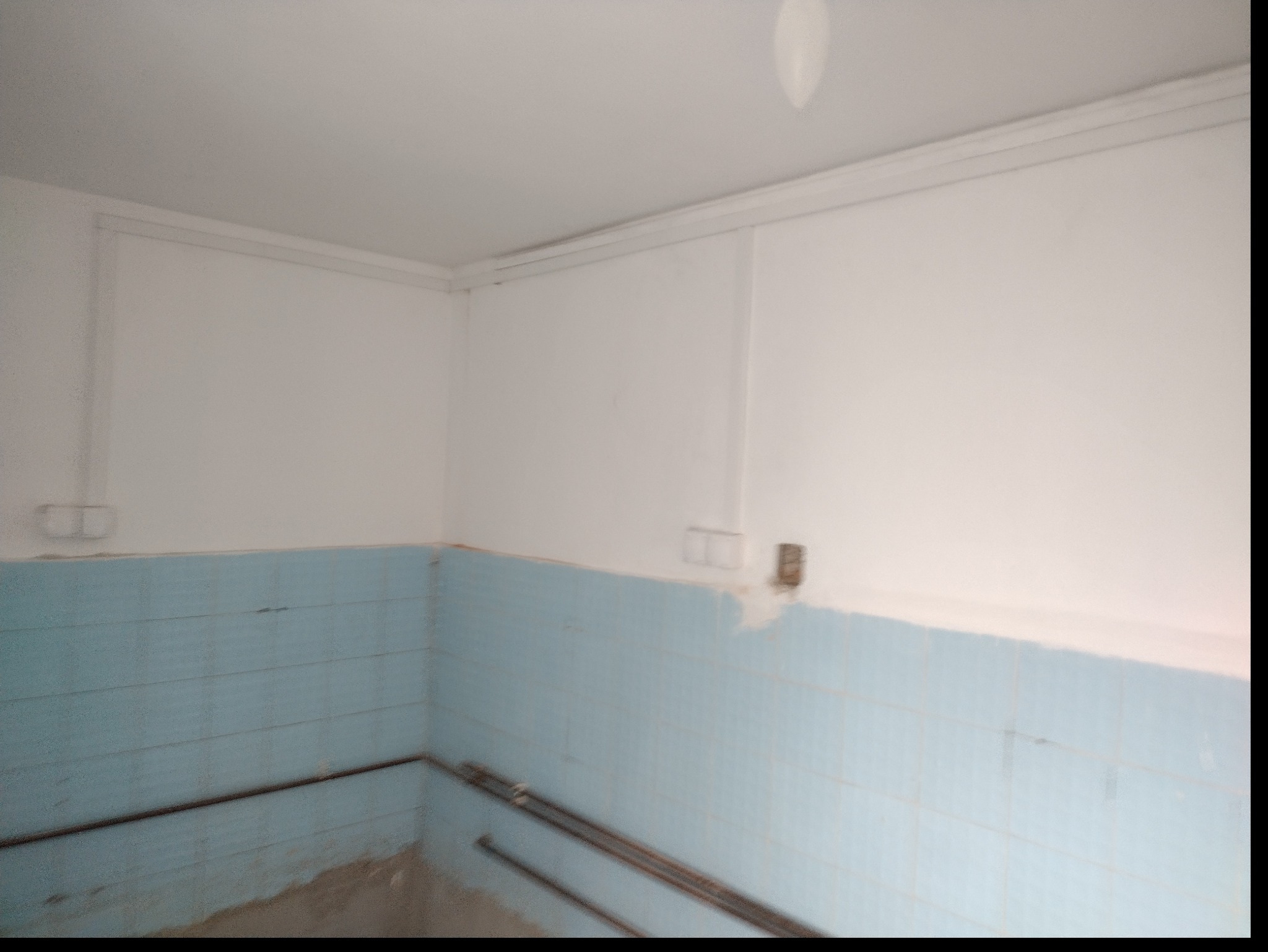 Wnętrze w trakcie remontu: Ściany wyłożone niebieskimi płytkami do połowy wysokości, widoczne przewody elektryczne wystające ze ściany, surowy stan wykończenia.