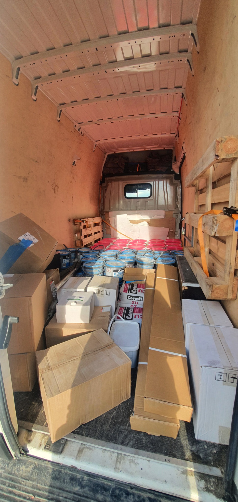 Wnętrze furgonetki wypełnione kartonami, wiadrami z farbą i paletami, przygotowane do transportu materiałów budowlanych.