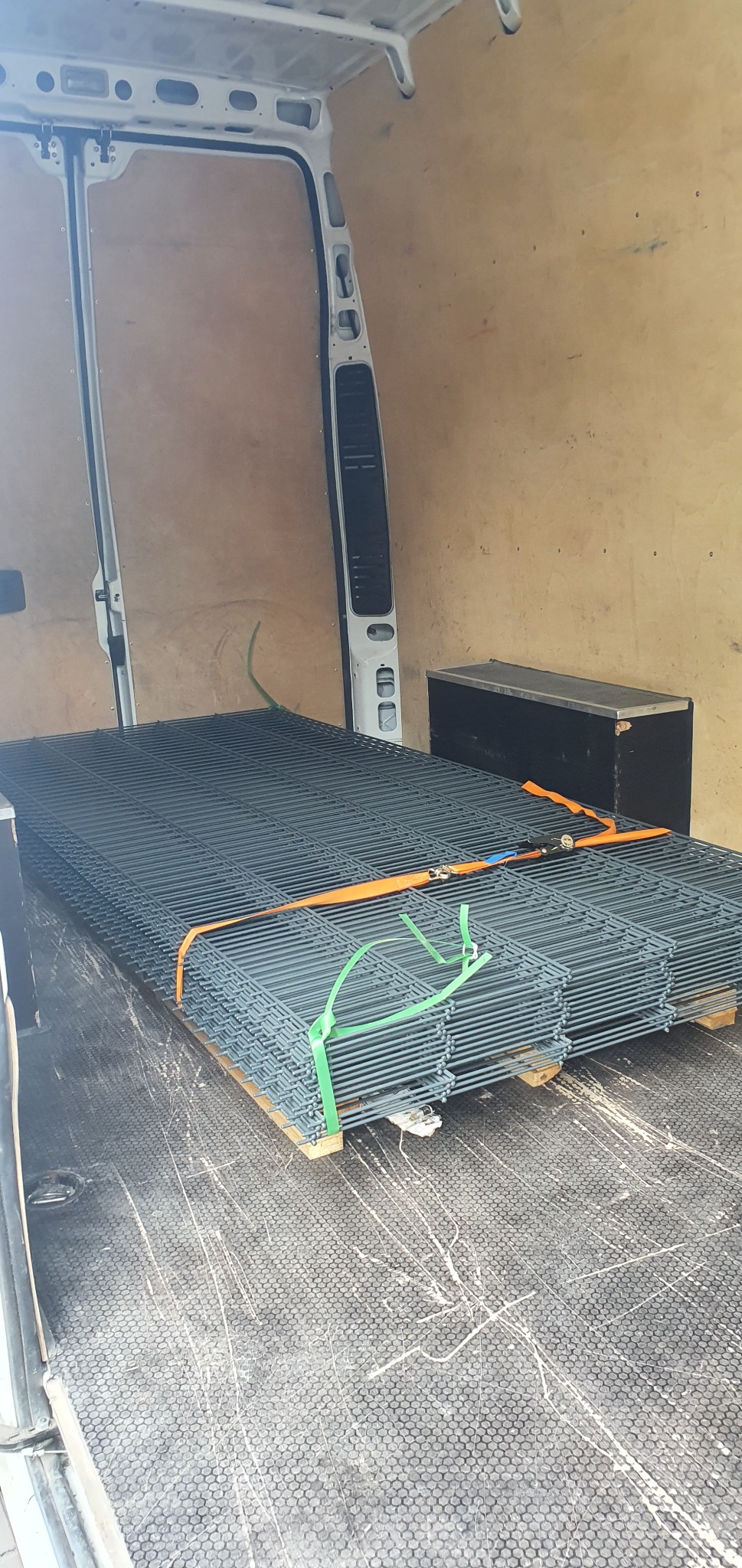 Paleta z panelami ogrodzeniowymi zabezpieczona pasami transportowymi wewnątrz furgonetki.