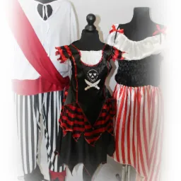 Trzy stroje pirackie na manekinach: męski z białą koszulą, czerwonym pasem i spodniami w czarno-białe paski, oraz dwa damskie - czarna sukienka z czaszką i czerwonymi paskami oraz bluzka...