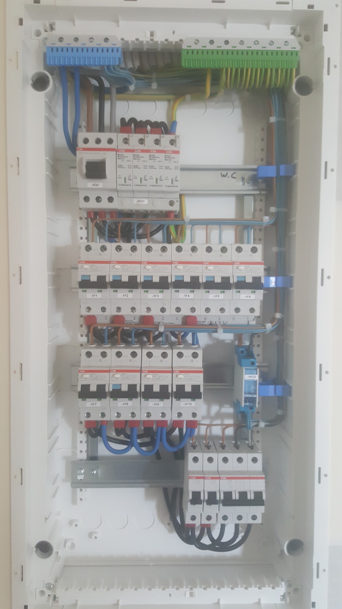 Rozdzielnica elektryczna z zainstalowanymi bezpiecznikami automatycznymi, zabezpieczeniami przepięciowymi i listwami zaciskowymi w kolorach niebieskim i zielonym, widoczne okablowanie w różnych...