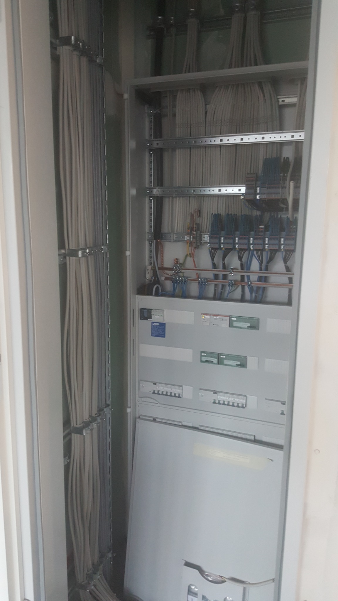 Otwarta szafa elektryczna z licznymi przewodami ułożonymi w wiązki, widoczne zabezpieczenia i elementy sterujące, instalacja w trakcie montażu.