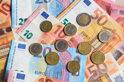 Rozrzucone banknoty i monety euro o różnych nominałach, ułożone na płaskiej powierzchni, oświetlone naturalnym światłem.