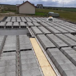 Wieniec stropowy z szalunkiem z płyty OSB i zbrojeniem stalowym, widok z góry na budowę domu w krajobrazie wiejskim.