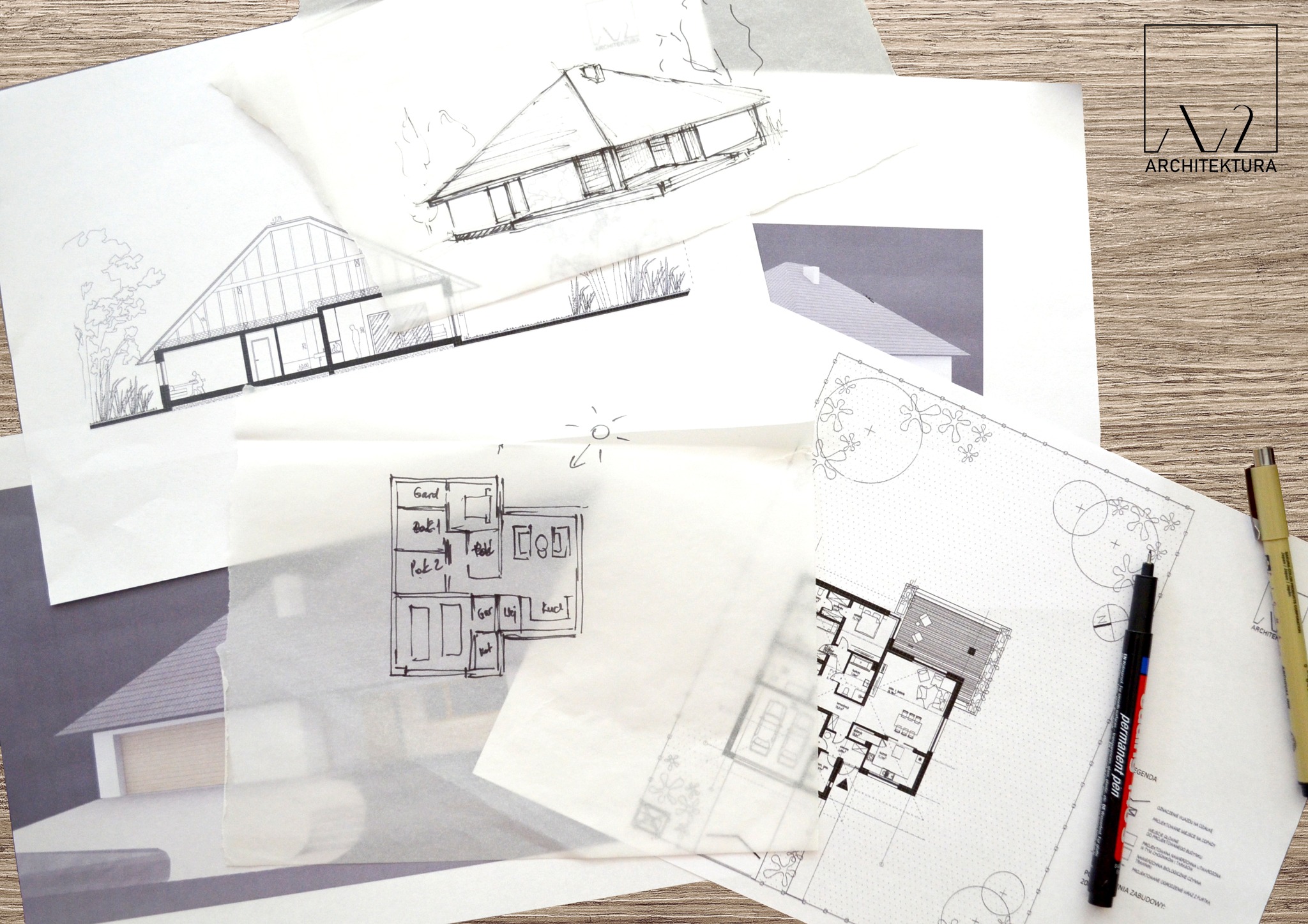 Ręcznie rysowane szkice i plany domu jednorodzinnego, w tym przekrój, rzut z góry i plan zagospodarowania terenu, ułożone na drewnianym stole, obok leżą dwa pisaki kreślarskie oraz logo firmy...