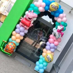 Wejście do przedszkola udekorowane łukiem z balonów w pastelowych kolorach z motywami Świnki Peppy, Minionka i jednorożca.