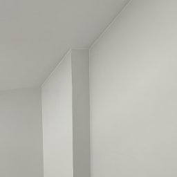 Profesmig Sywester Tempski - Wnętrze pokoju po malowaniu na biało, widoczne ślady farby na podłodze, narożnik ściany i gniazdko elektryczne.