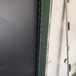 Montaż ościeżnicy drzwiowej przy ścianie z widocznymi śladami po wcześniejszych pracach, poziomica przyłożona do ściany, zielona linia lasera wyznacza poziom.