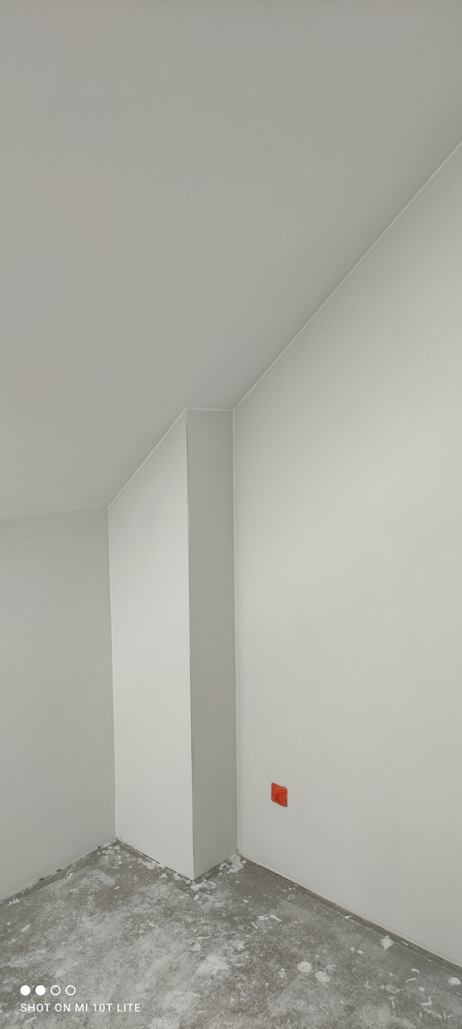 Wnętrze pokoju po malowaniu na biało, widoczne ślady farby na podłodze, narożnik ściany i gniazdko elektryczne.