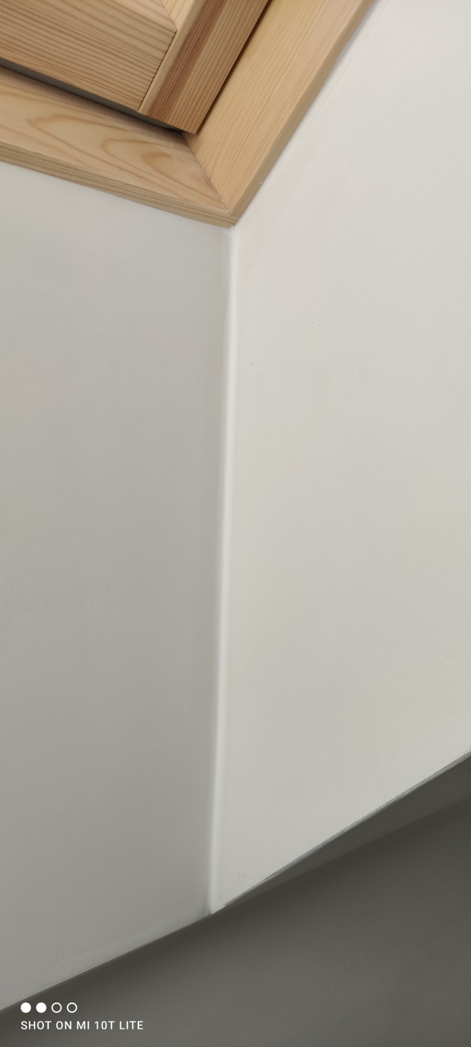 Pomieszczenie po malowaniu na biało, widoczny fragment drewnianej ramy okiennej i gładka powierzchnia ściany.