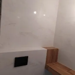 Wykończona łazienka z marmurowymi płytkami, drewnianym siedziskiem i czarnym przyciskiem spłuczki.