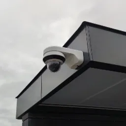 Kamera IP kopułkowa zamontowana na ciemnej, metalowej konstrukcji pod pochmurnym niebem.