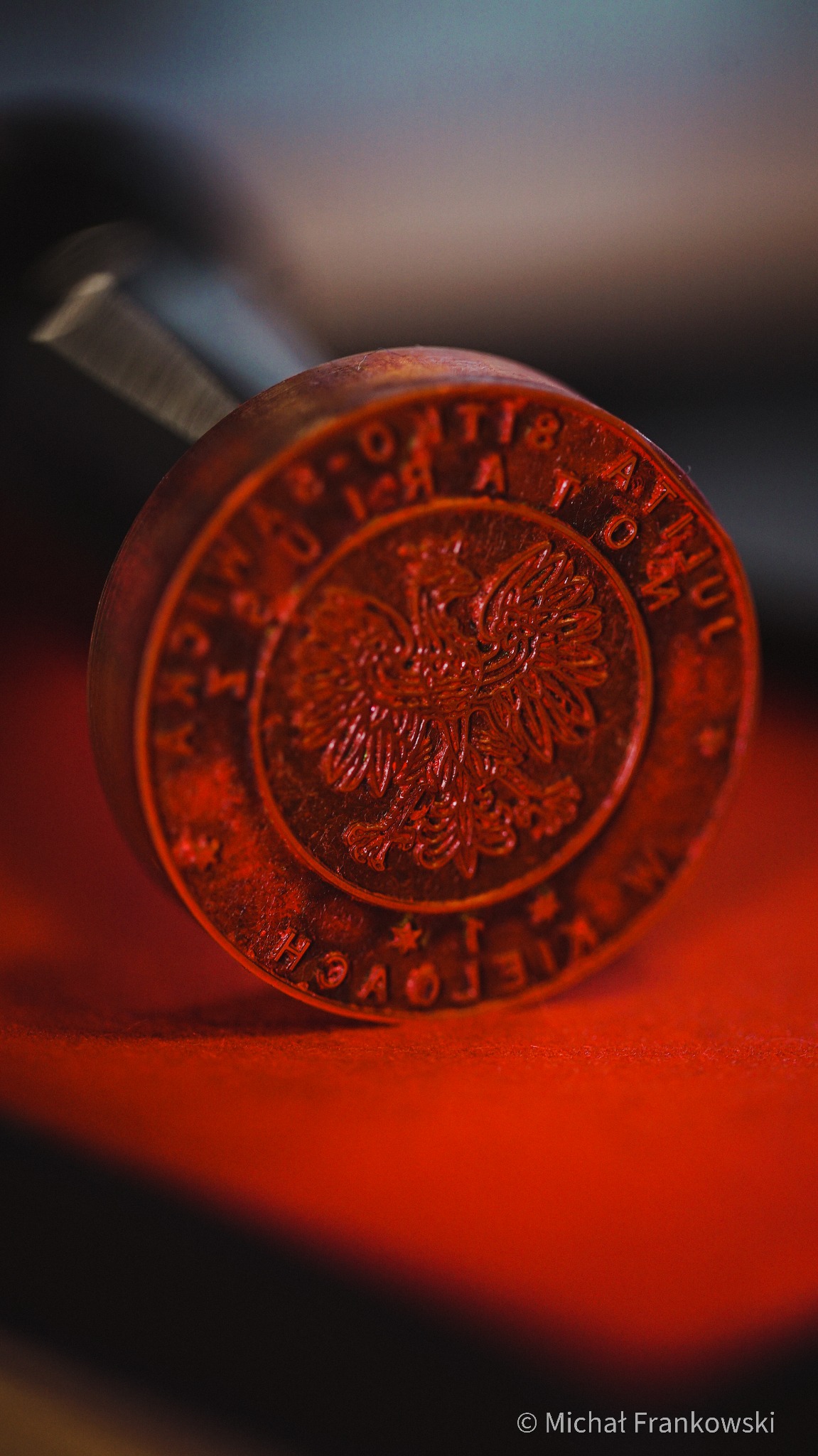 Metalowa pieczęć z orłem w koronie i napisem 'Rzeczpospolita Polska Kielce' na czerwonym podłożu, ujęcie z bliska.