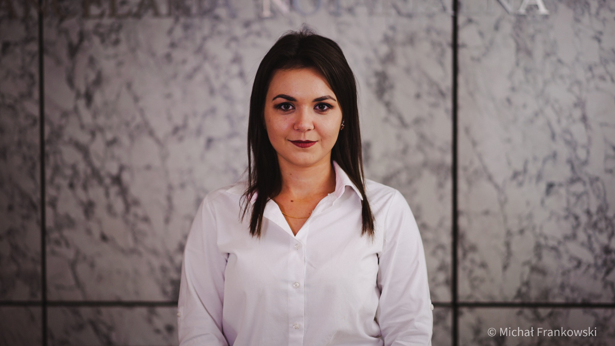 Portret kobiety w białej koszuli na tle marmurowej ściany z napisem kancelarii.