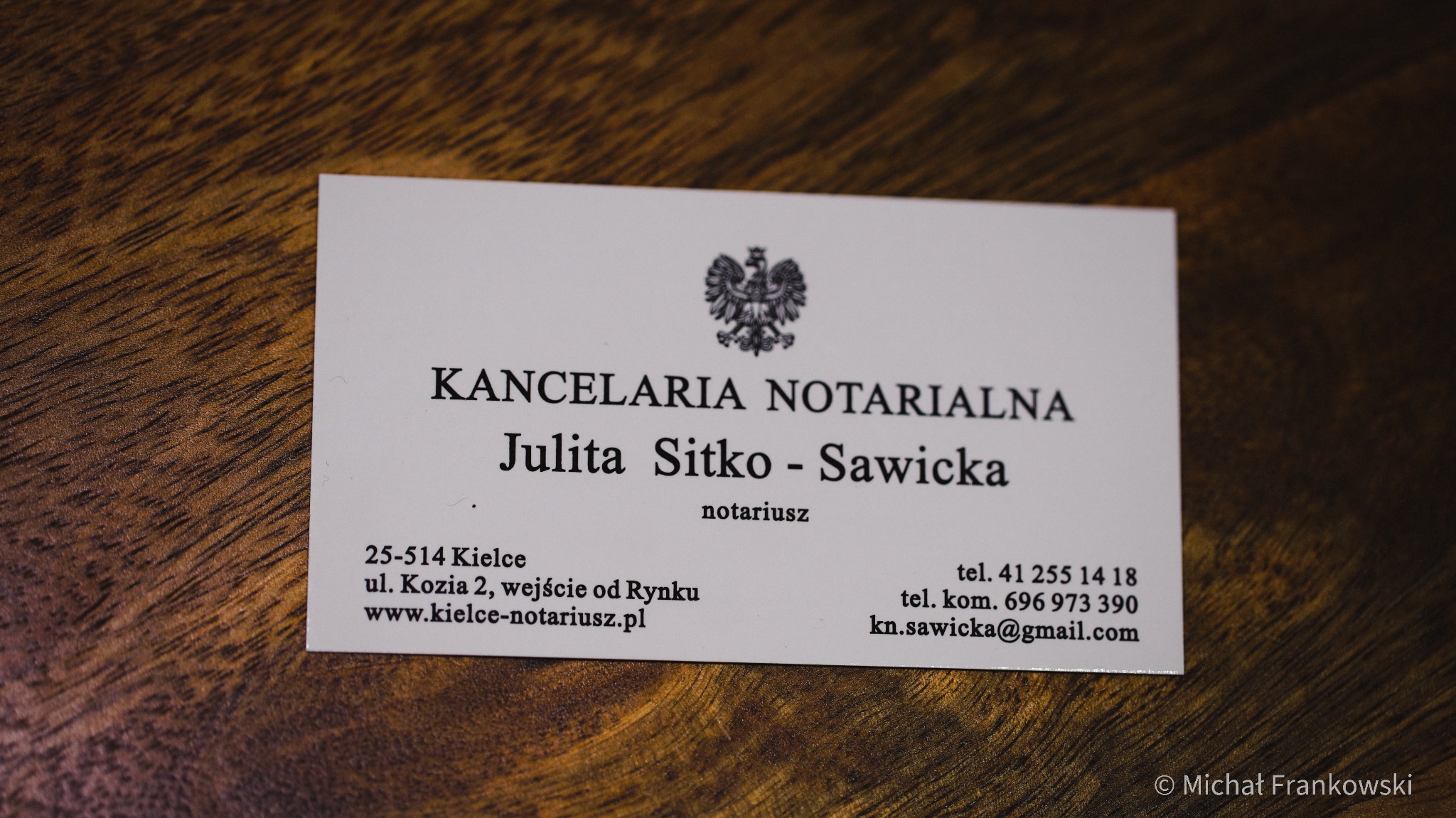 Wizytówka Kancelarii Notarialnej Julita Sitko-Sawicka z adresem w Kielcach, położona na drewnianym blacie.