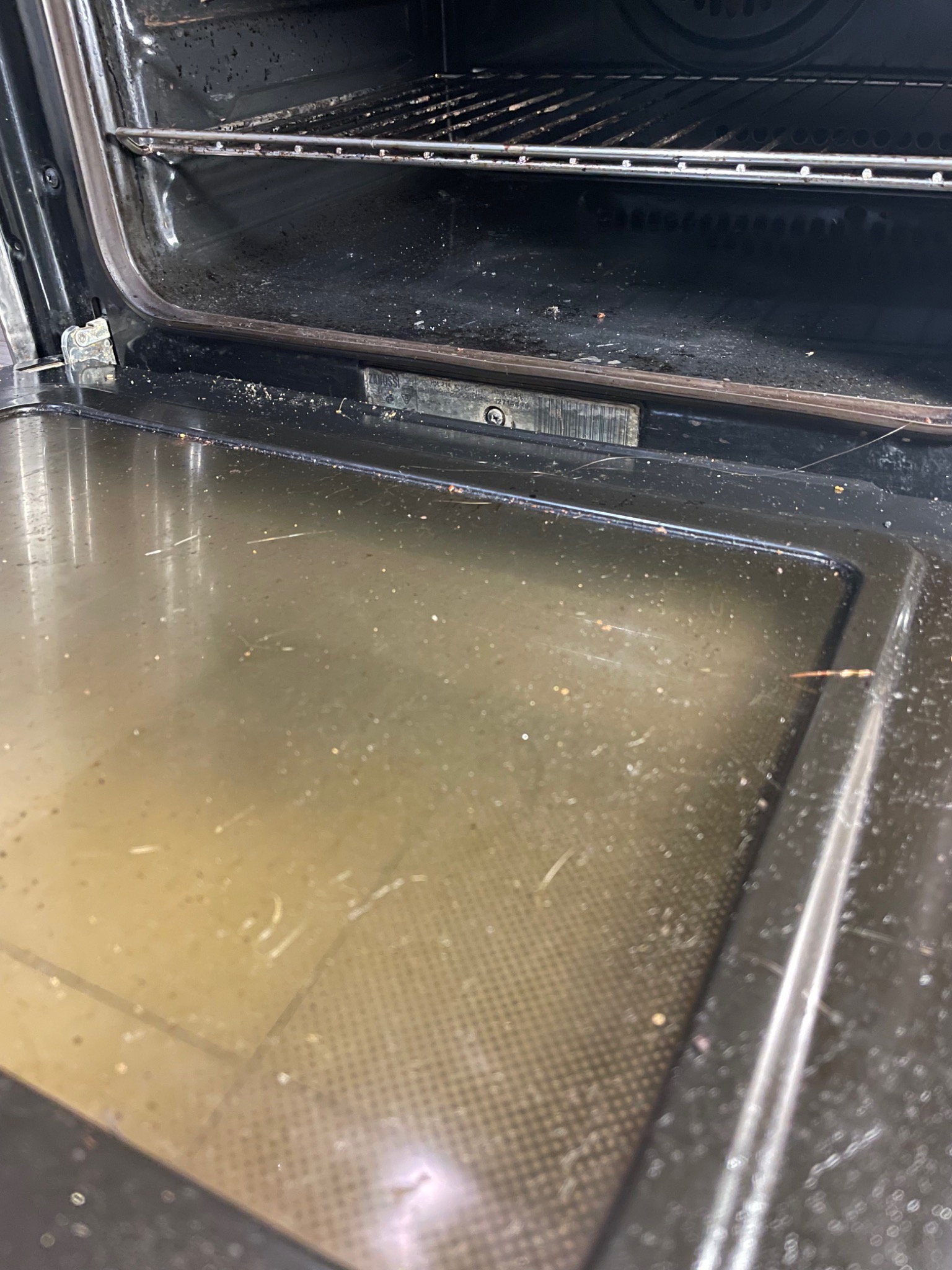 Wnętrze bardzo brudnego piekarnika z resztkami jedzenia i tłuszczu na dnie oraz na ruszcie.