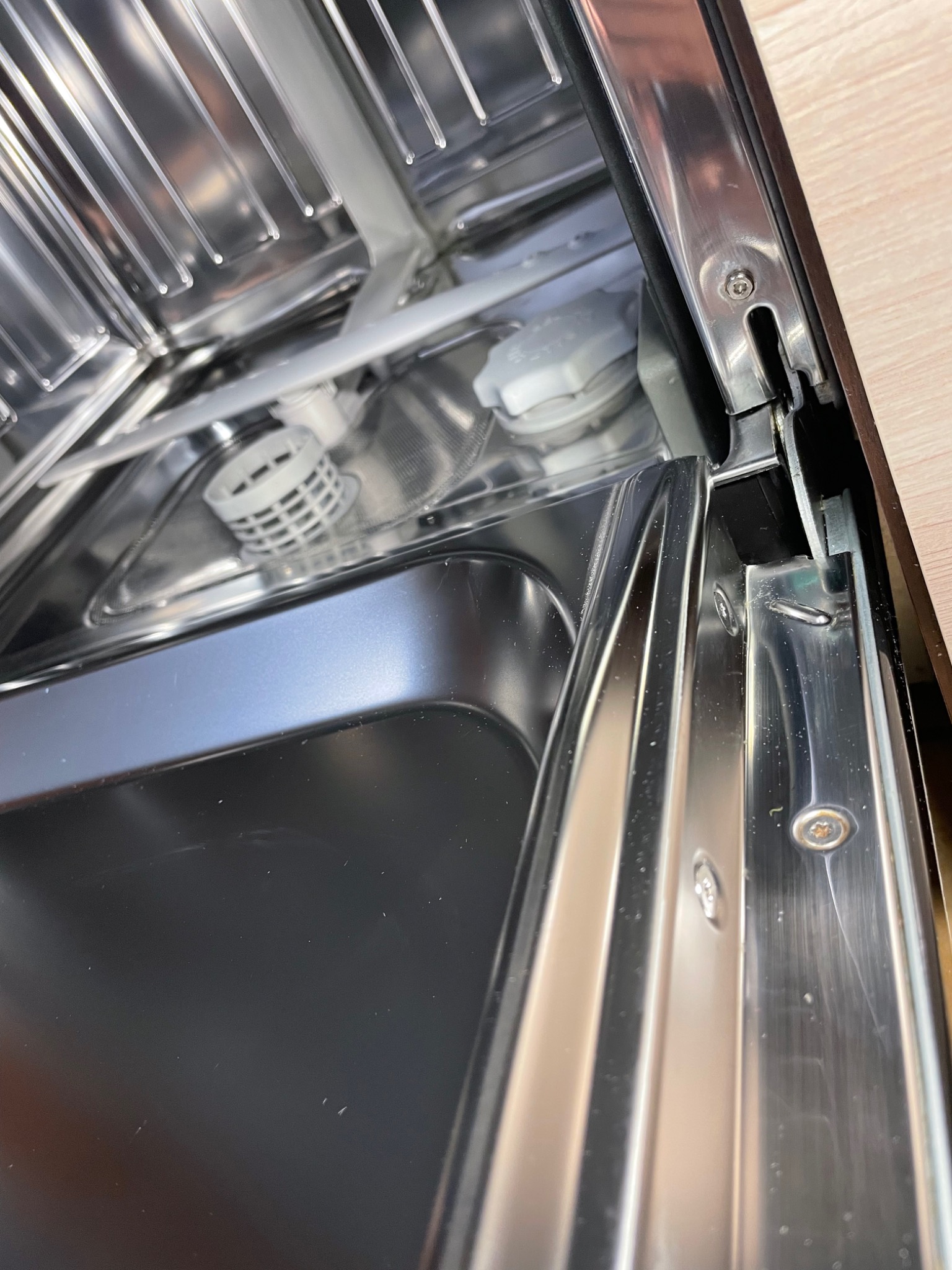 Wnętrze otwartej, pustej zmywarki, widoczne metalowe elementy, filtr i dozownik nabłyszczacza.