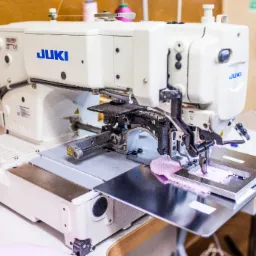 Profesjonalna maszyna szwalnicza JUKI w trakcie pracy z różowym materiałem, zbliżenie na mechanizm igły i stopki dociskowej.