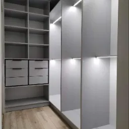 Wnętrze szafy wnękowej z szufladami, półkami i oświetleniem LED, wykończonej w odcieniach szarości, z podłogą imitującą drewno.