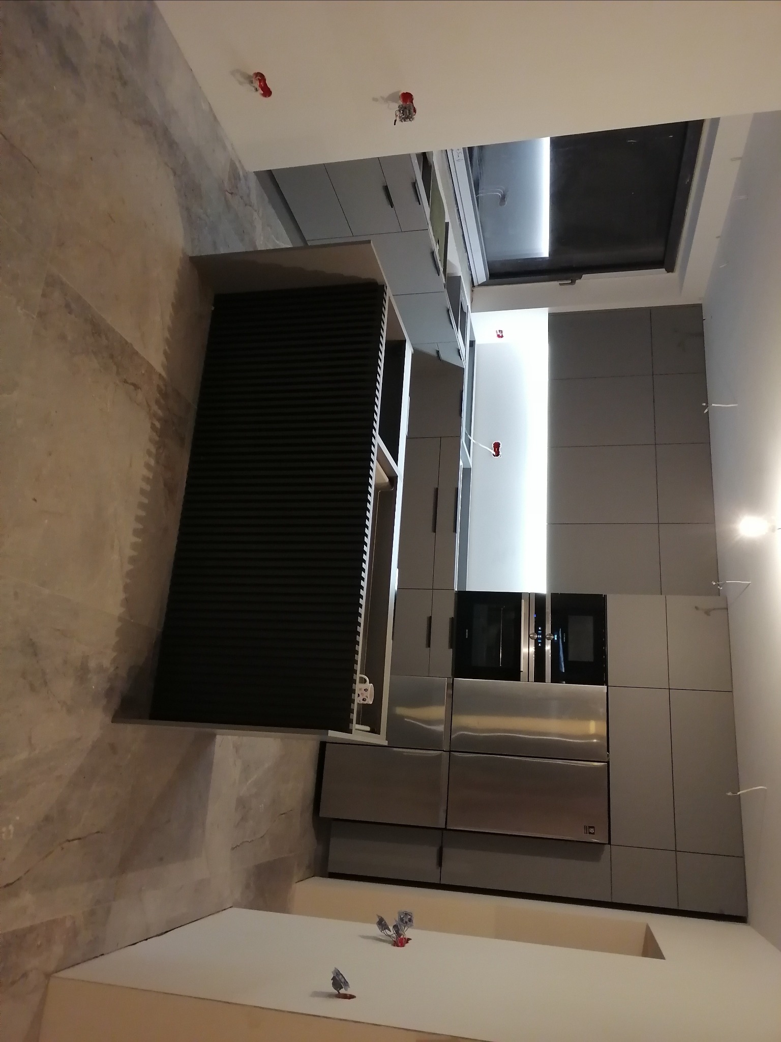 Szara zabudowa kuchenna w trakcie montażu, widoczne niedokończone wykończenia i wystające kable elektryczne.