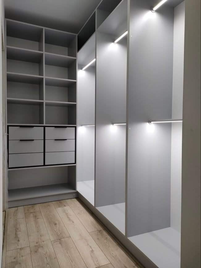 Wnętrze szafy wnękowej z szufladami, półkami i oświetleniem LED, wykończonej w odcieniach szarości, z podłogą imitującą drewno.