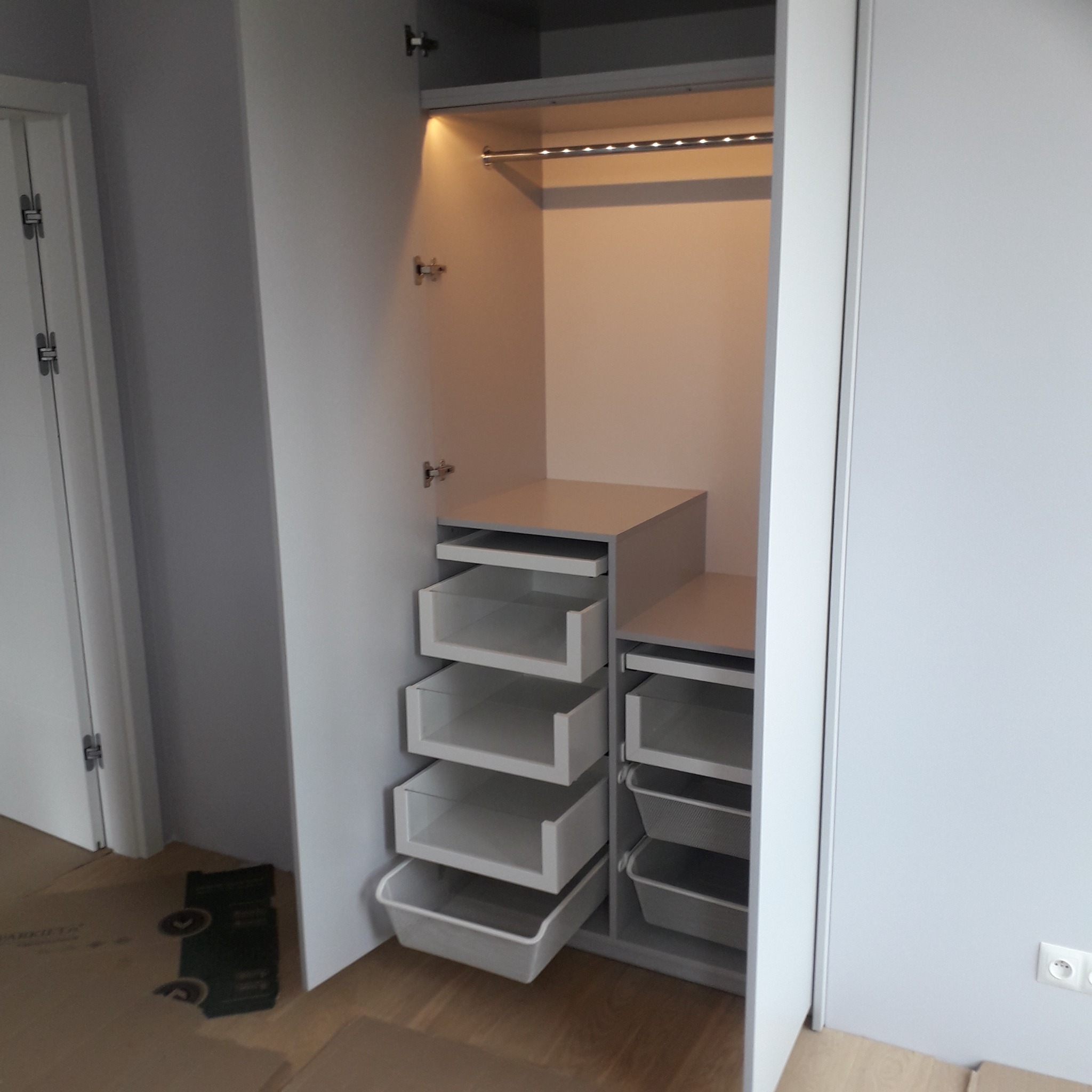 Wnętrze szafy wnękowej z szufladami i oświetleniem LED, widoczne również fragmenty drzwi i podłogi.