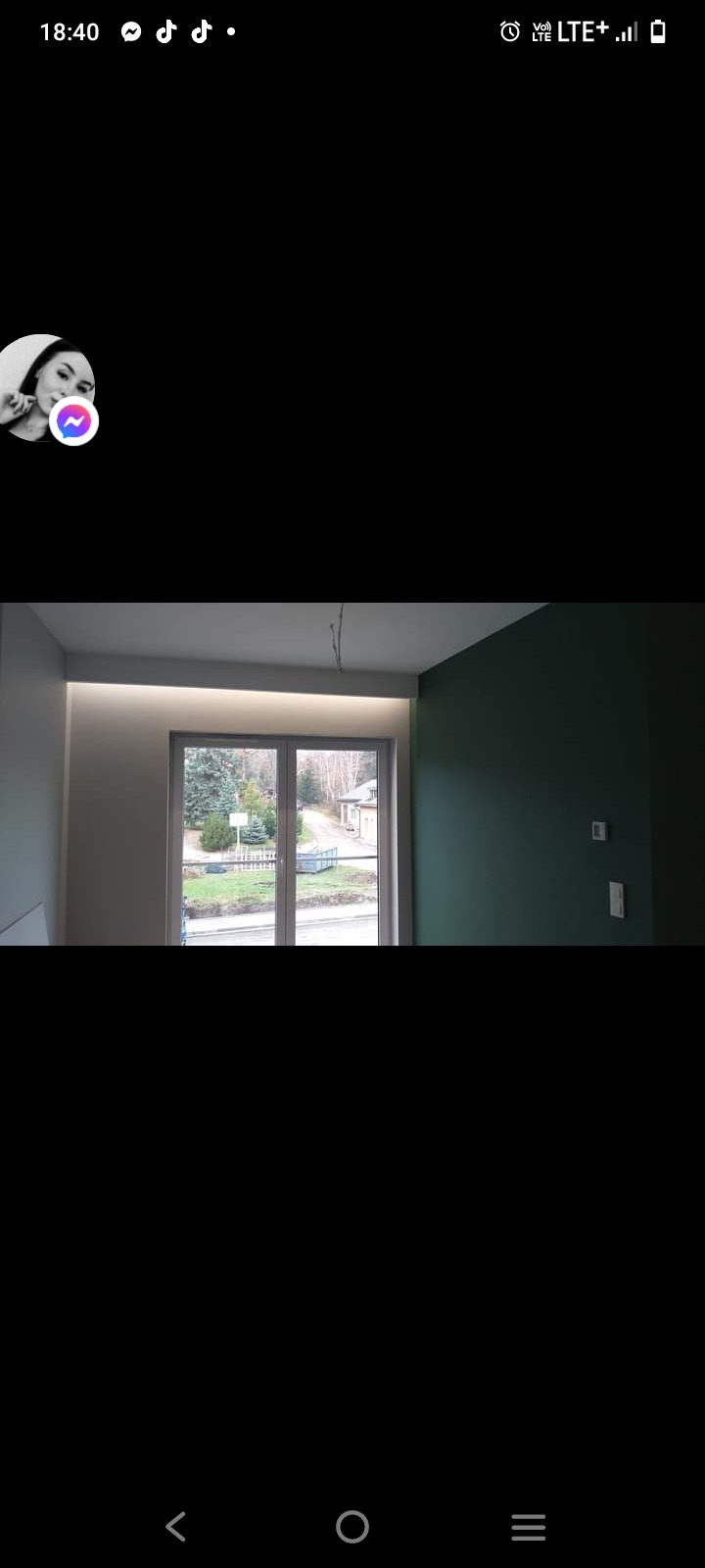 Wnętrze pokoju po remoncie: ściany pomalowane na szaro i butelkową zieleń, okno z widokiem na ogród, ukryte oświetlenie sufitowe.