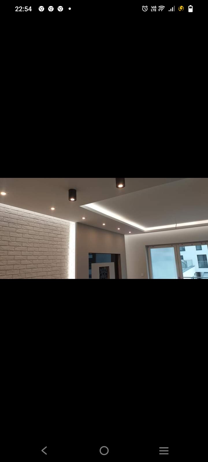 Nowoczesne wnętrze z ceglaną ścianą, podwieszanym sufitem z oświetleniem LED i czarnymi reflektorami punktowymi.