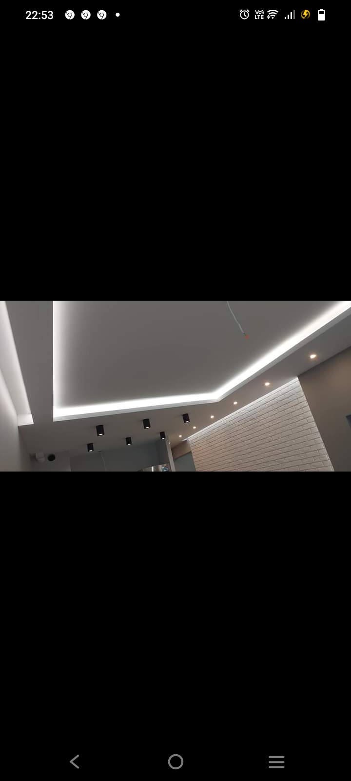 Nowoczesne oświetlenie biurowe: podwieszany sufit z listwami LED i punktowymi lampami, ściana wykończona cegłą dekoracyjną, widok z dołu.