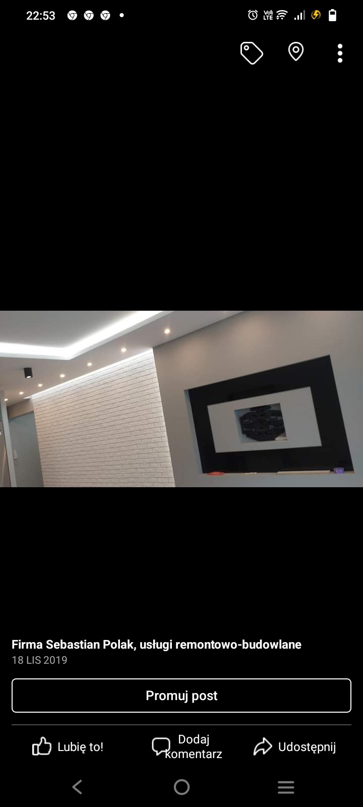 Biała ściana z cegły dekoracyjnej z oświetleniem punktowym na suficie podwieszanym i czarna rama dekoracyjna na szarej ścianie w nowoczesnym wnętrzu.