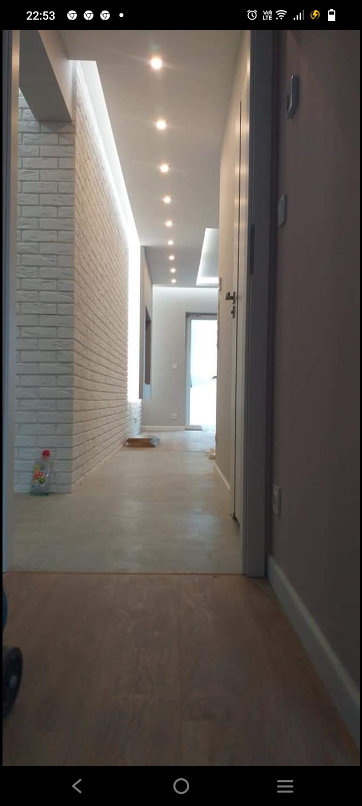 Korytarz po odświeżeniu: ściana z białej cegły, podłoga imitująca drewno, sufit z oświetleniem punktowym, widoczny środek czyszczący na podłodze.