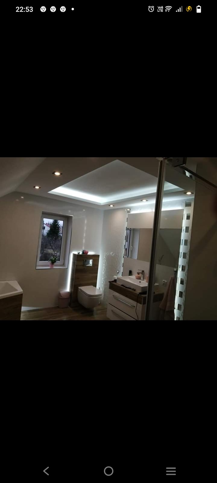 Nowoczesna łazienka z podświetlanym sufitem, drewnianymi akcentami i kabiną prysznicową ze szklanymi elementami dekoracyjnymi.