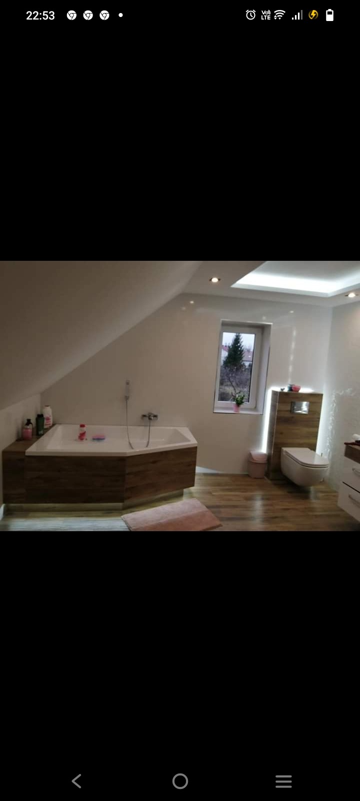 Nowoczesna łazienka na poddaszu z drewnianą zabudową wanny, podświetleniem LED, wiszącą toaletą i drewnianą podłogą.