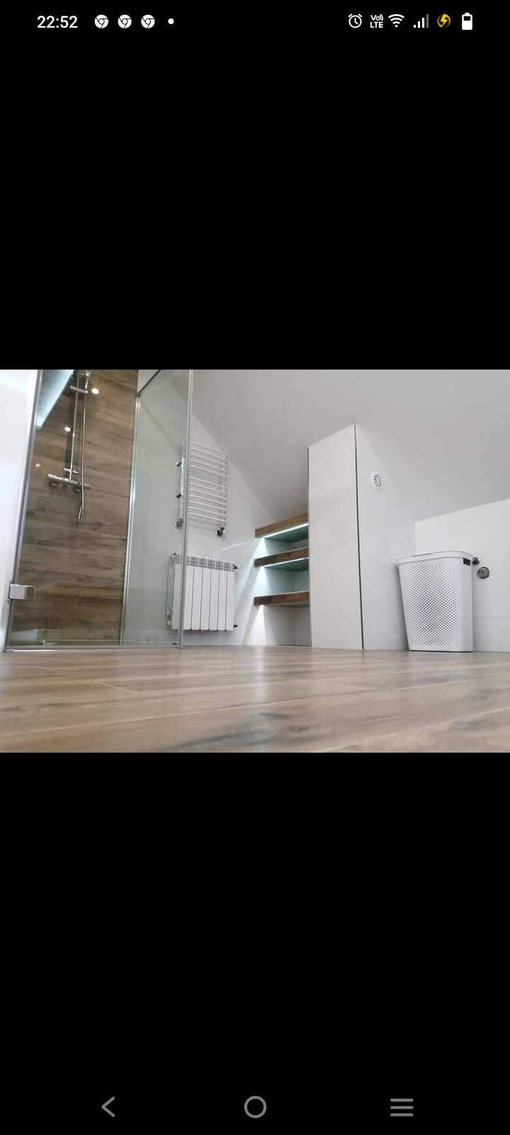 Nowoczesna łazienka na poddaszu z kabiną prysznicową z drewnopodobnymi płytkami, grzejnikiem drabinkowym, białym grzejnikiem panelowym, podświetlanymi półkami i koszem na pranie.