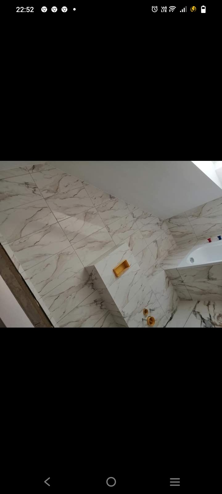 Ściany łazienki wyłożone białymi płytkami z marmurkowym wzorem, widoczne instalacje wodne i fragment wanny.