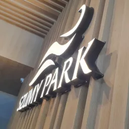 Podświetlany szyld z nazwą 'SZUMNY PARK' w czarno-białej kolorystyce, zamontowany na drewnianej ścianie z pionowymi panelami.