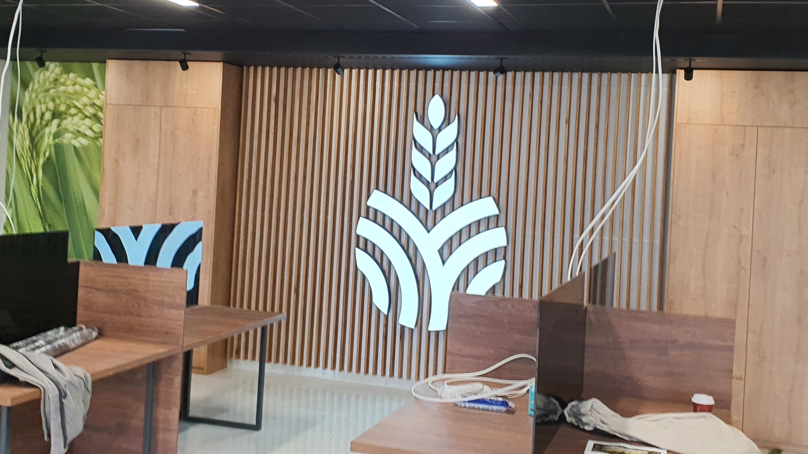 Biuro z drewnianą ścianą z logo w kształcie kłosa zboża, widoczne biurka i elementy dekoracyjne.