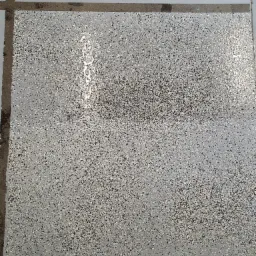 Szara posadzka z żywicy epoksydowej z drobnymi, czarnymi, białymi i beżowymi elementami dekoracyjnymi, widoczne fragmenty butów w dolnej części kadru.