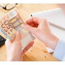 Dłonie liczą plik banknotów 50 euro na biurku z kalkulatorem i notatnikiem, widoczne okulary w tle.