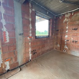 MAT-KAS Mateusz Kasperkiewicz - Surowy stan: instalacja elektryczna w nowym budynku z czerwonej cegły. Widoczne kable, puszki elektryczne i oznaczenia na ścianach. Podłoga wylewka.