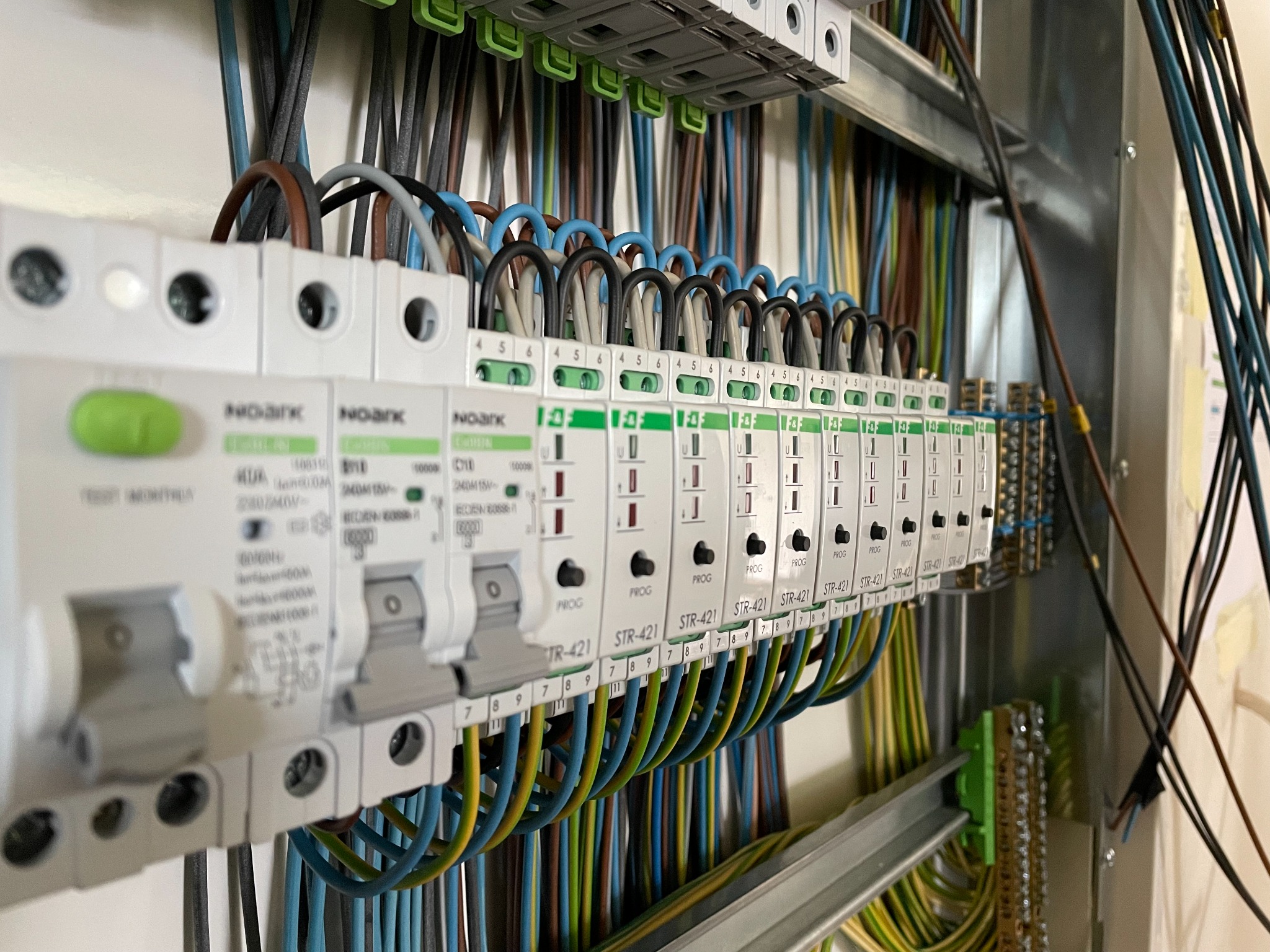 Rozdzielnica elektryczna z zamontowanymi ogranicznikami przepięć Noark STR-421, z podłączonymi przewodami w różnych kolorach. Widok z boku, oświetlenie naturalne.