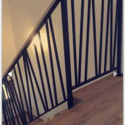 Nowoczesna balustrada schodowa z czarnymi, pionowymi prętami i jasnoszarą poręczą, zamontowana na drewnianych schodach w jasnym wnętrzu.