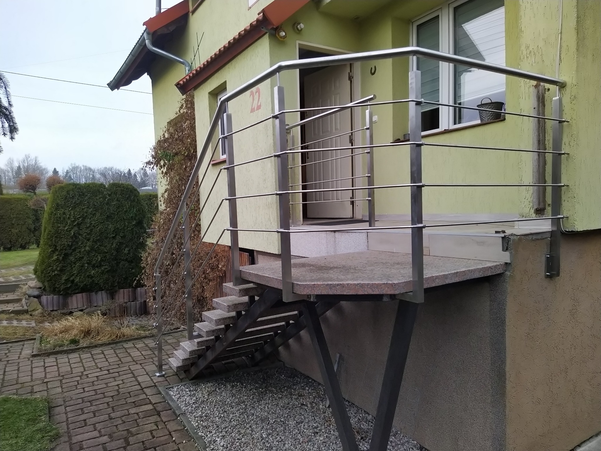 Zewnętrzne schody z granitu i balustrada ze stali nierdzewnej prowadzące do wejścia domu z numerem 22.