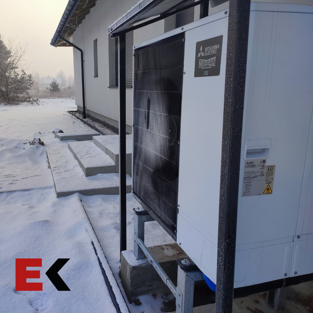 Zewnętrzna jednostka pompy ciepła Mitsubishi Zubadan, zamontowana na betonowych podstawach przy ośnieżonym budynku jednorodzinnym, widoczna instalacja.